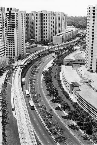 Schwarz-weiß Fotografie einer sich durch Wohnhausblöcke schlängelnden Autobahn aus der Vogelperspektive
