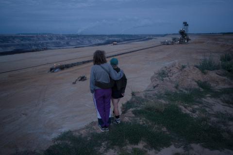 Zwei sich umarmende Personen schauen von einer Klippe hinter ins Tal
