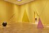 Der Raum ist mit gelben Tüchern behangen. Darin eine Kugel und ein Dreieck. Von der Decke hängen Stäbe, die wie eine Treppe angeordnet sind.