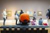 Ein Kind mit orangener Mütze und Audio-Guide Kopfhörern sitzt in einem Ausstellungsraum und betrachtet mit dem Rest seiner Gruppe die Kunstwerke.